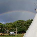 The sun shines even when it rains! A rainbow vivid in the dark and brooding sky above WoWo campsite, the striking white canvas of the tipi is in the righthand side of the picture. A great place to shelter when the weather turns sour and you need a warm place to get cosy next to the fire.