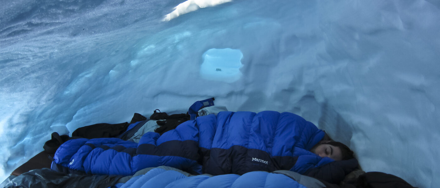 Sleeping in a snow shelter- the warm sleeping bags and thick mats keep the students warm. The glow of the pale blue ice is above.