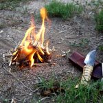 Small fire burning next to a wooden handled bushcraft knife and fire striker which we just used to light the fire