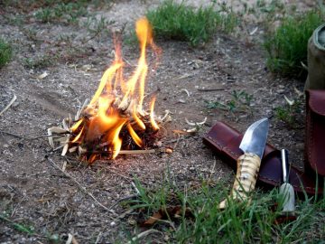 Small fire burning next to a wooden handled bushcraft knife and fire striker which we just used to light the fire