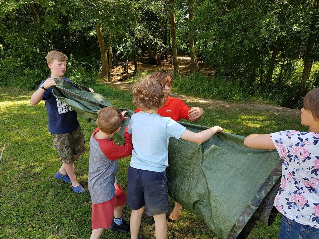 Children folding up a tarpaulin ready to use next time. Being careful with equipment is essential when in a survival situation.